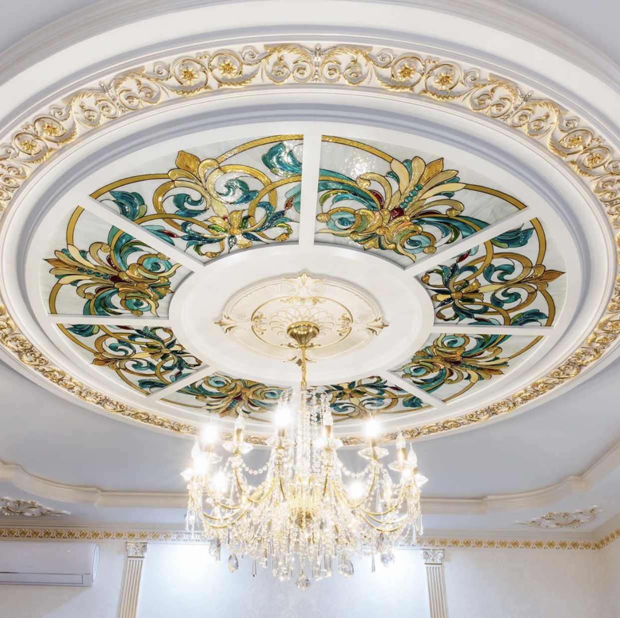 Gold chandelier under stained-glass ceiling with ornate plaster ring and warm LED glow